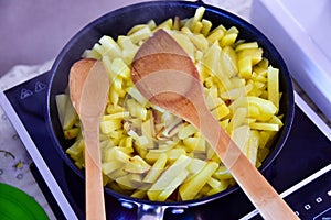 cooking in the kitchen. two wooden spoons and fried potatos in a cast iron skillet on the stove