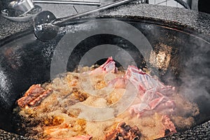 cooking lamb meat in boiling cauldron for traditional oriental Uzbek pilaf in kitchen of a restaurant in Uzbekistan