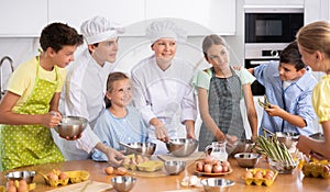 During cooking lesson, female cook tells children about culinary rules, guy assistant helps child