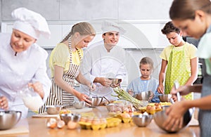 During cooking lesson, male cook tells children about culinary rules, woman assistant helps child