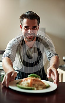 Cooking is love made edible. Cropped portrait of a handsome young man serving food in the kitchen at home.