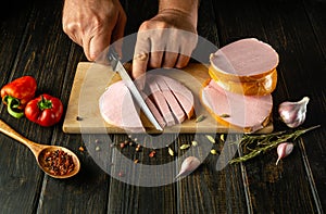 Cooking a meat dish. Slicing sausage by the hands of a cook on a cutting board. Work environment on kitchen table with spices and