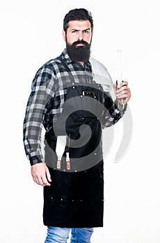 Cooking meat in park. Bearded hipster wear apron for barbecue. Roasting and grilling food. Man hold cooking utensils