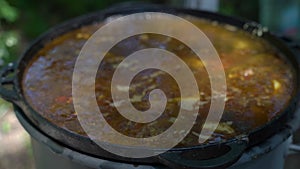 Cooking meat soup in a large cauldron on a fire. Slow motion