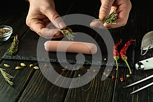 Cooking Munich sausage. The chef hands add fragrant rosemary to the sausage on the kitchen table before baking in the kitchen.