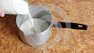 Cooking oatmeal, a woman pours milk into the pan, close-up