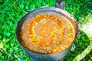 Cooking outdoors. Solyanka, meat hodgepodge soup in a large pot photo