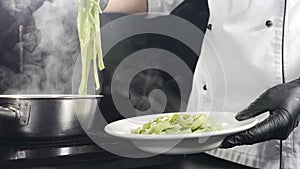 Cooking pasta in Italian restaurant. Chef serving cooked pasta on plate. Slow motion. Vapour or White steam rising up on