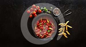Cooking pasta penne with tomato sauce and basil served on iron cast pan. Black slate background, top view