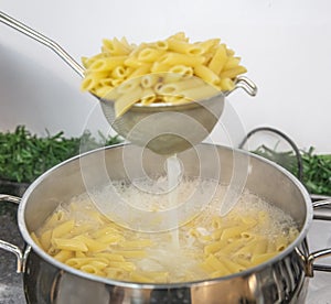 Cooking Pasta pour the penne pasta into a metal pot of boiling water. Boiled penne on a steel colander, in a cooking class