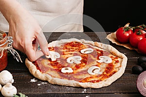 Cooking pizza. Hands adding fresh mushrooms to pizza. Pizza ingredients on the wooden table