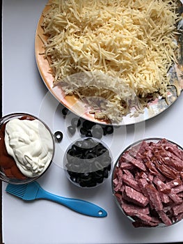 Cooking pizza. Ingredients are laid out on the dough: cheese, olives, sausages and champignons.