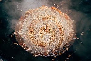 Cooking plov in the cauldron. Rice, meat, onions and carrots in