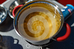 Cooking on a portable gas stove, on a folding table in the background of camping in the woods. Spaghetti in a pot on a gas burner