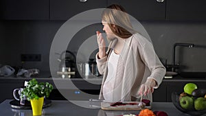 Cooking during pregnancy. A pregnant woman cuts red beet with a kitchen knife. A woman sniffs a head of garlic and feels