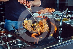 Cooking process in an Asian restaurant. Cook is fry vegetables with spices and sauce in a wok on a flame.