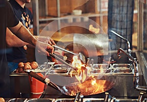 Cooking process in an Asian restaurant. Cook is stirring vegetables in a wok on a flame.