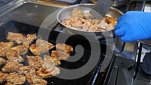 The cooking process in the kitchen of the restaurant, the chef in blue gloves fry the meat in a frying pan and grill in