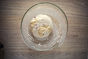 a ball of dough in a transparent bowl on a wooden table