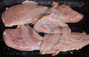 Cooking raw chicken fillets in a hot frying pan on stove, fresh meat on rustic grilling pan. Extreme close up real kitchen cooking