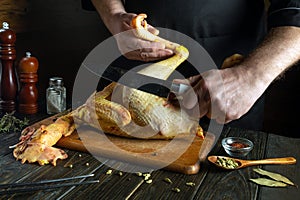 Cooking raw rooster on the kitchen table. A knife in the chef hand for slicing chicken for preparing dinner