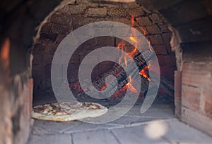 Cooking real pizza in a brick oven. Wood and fire are burning