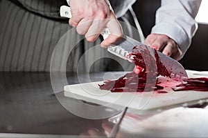 Cooking in a restaurant kitchen. Closeup of hand with knife cutting fresh vegetable. Young chef cutting beet on a white