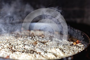 Cooking Rice for pilaw or paella in iron cauldron over open fire. Smoke and steam. Tasty food preparing outdoor process