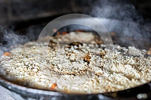 cooking Rice for pilaw or paella in iron cauldron over open fire. Smoke and steam. Tasty food preparing outdoor process background