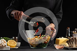Cooking salad, mixing in a large transparent plate. On a black background with ingredients. Cooking, gastronomy, home recipes.