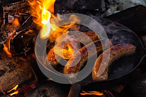 Cooking sausages in cast iron skillet on campfire while camping. Good and positive campfire food.