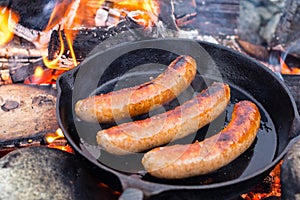 Cooking sausages in cast iron skillet on campfire while camping. Good and positive campfire food.
