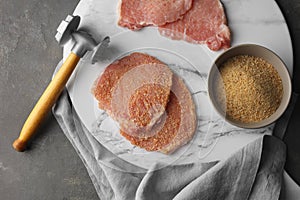 Cooking schnitzel. Raw pork chops, bread crumbs and meat mallet on grey table, top view