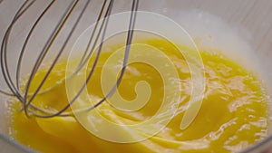 Cooking scrambled eggs. Close up shot of chef mixing egg yolks with metal whisk in bowl, preparing dough at kitchen