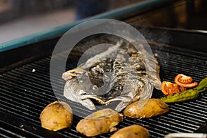 Cooking sea bass and vegetables. Grilling fish with chili potatoes and tomato.