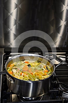 Cooking soup in a metal pan on a gas stove, chicken vegetable soup with bow tie pasta