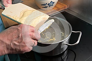 Cooking spaetzle, hands of a man are scraping  homemade egg pasta dough from a wooden board into boiling water, typical dish in