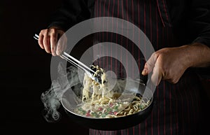 Cooking spaghetti with spices and seasonings in a pan by the hands of a chef. Recipe or menu for hotel on black background