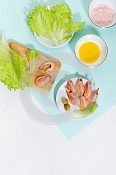 Cooking of spring salad with shrimps, green olive, greens, olive oil, ingredients on pastel minty background with shadow in hard.