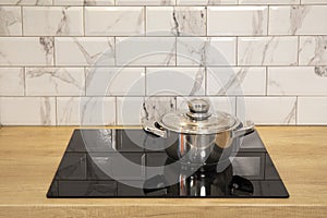 Cooking stainless still pan at modern kitchen induction cooker hob and wooden counter and white tile backsplash