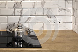 Cooking stainless still pan at modern kitchen induction cooker hob and wooden counter and white tile backsplash