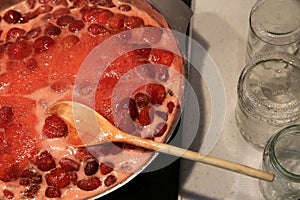 Cooking strawberry jam in a large bowl at home. Wooden spoon in a bowl with jam. Empty glass jars for jam.