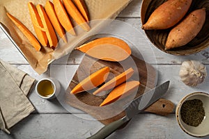 Cooking sweet potato wedges, raw sweet potatoes sliced on cutting board.