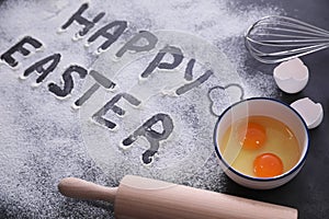 Cooking tools, eggs and words Happy Easter written in flour on black table. Baking cake