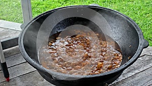 Cooking traditional real Uzbek pilaf during a stewing lamb in a huge cauldron with lots of steam outside