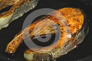 Cooking two fried salmon steaks in the black pan