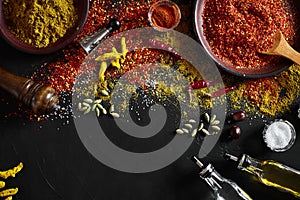 Cooking using fresh ground spices with big and small bowls of spice on a black table with powder spillage on its surface