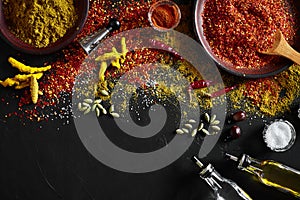 Cooking using fresh ground spices with big and small bowls of spice on a black table with powder spillage on its surface