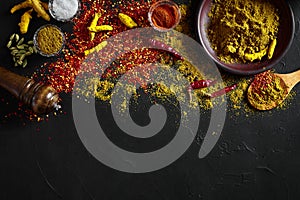 Cooking using fresh ground spices with big and small bowls of spice on a black table with powder spillage on its surface