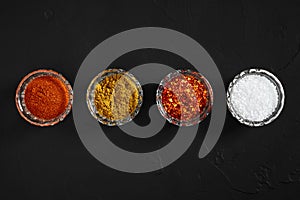 Cooking using fresh ground spices with four small bowls of spice on a black table overhead view with copyspace